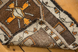 Folded vintage Oushak rug corner reveals brown pile, tangerine patterns, and reverse with processing numbers.