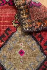 Distressed Oushak rug close-up, showing even pile wear, hot pink, red, and brown geometric patterns.