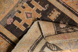 Curled distressed Oushak rug showing geometric charcoal, orange, pink patterns and woven reverse.