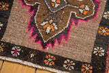 Distressed Oushak rug corner featuring a chocolate brown border, hot pink outline, and tangerine floral motifs.