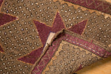 Distressed Oushak rug corner showing aubergine pattern, speckled brown field, and side selvage.