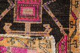 Decorative distressed Oushak rug detail showing fuchsia, saffron, aubergine plant motifs on charcoal.