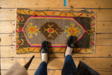 Distressed Oushak rug's textured pile with central brown medallion, saffron and hot pink motifs.