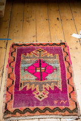 Distressed vintage Oushak rug corner showing hot pink field, tangerine vine border, and geometric patterns.