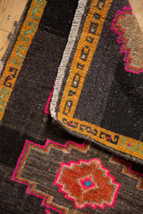 Distressed Oushak rug with charcoal brown ground, saffron yellow border, and hot pink stepped finial.