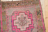Oushak rug corner with hot pink hooked rams horn motif, dark brown selvage, distressed pile.