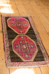 Distressed vintage Oushak rug corner, raspberry red motif on dark brown field with fringed edge.