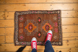 Distressed Oushak rug in chestnut brown, vibrant orange and pink geometric motifs, with red sneakers.