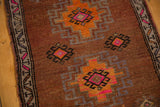 Distressed Oushak rug close-up: rich brown ground with tangerine, pink, and grey geometric motifs.