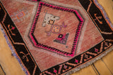 Distressed Oushak rug showing geometric motifs in pale grapefruit red, black, and bright pink.