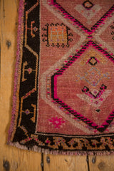 Distressed Oushak rug corner: geometric motifs, charcoal border, pale grapefruit red, and bright pink.