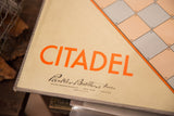 Close view of the vintage Citadel game board's orange title and maker's script.