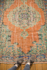 Distressed Oushak rug detail: worn burnt orange pile, mint, blue, ivory pattern, fringed end.