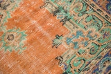 Distressed texture of a vintage Oushak rug, showing burnt orange and mint green motifs.