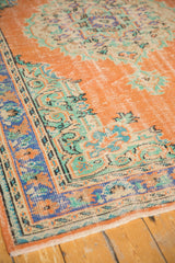 Distressed Oushak rug corner with mint green and burnt orange curvilinear patterns.