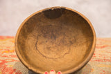 The hand-carved interior of a vintage African bowl showing dark aged patina and a crack on the rim.