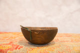 Hand-carved primitive African wooden bowl displaying aged texture, deep brown patina, and green tie.