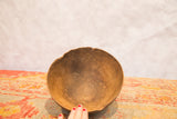 Hand touching vintage African wooden bowl's dark interior and irregular, cracked rim.
