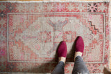 Distressed Turkish Oushak rug corner showing brick red, blush pink, and beige serpent motifs.