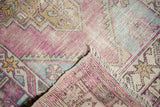Distressed Oushak rug corner showing worn pile, exposed foundation, and fringe.