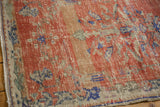 Distressed vintage Oushak rug corner, showing worn red pile, blue motifs, and visible foundation.