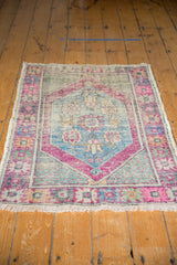 Distressed vintage Oushak rug's lower corner, displaying a diamond spandrel with seed motifs in bright pink, blue, and mint green.