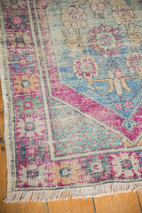 Distressed Oushak rug corner: vibrant pink, blue, mint green patterns, visible wear, and fringe.