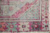Distressed Oushak rug corner with blush, mint green, aubergine patterns, and knot wear.