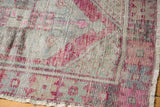 Close-up of vintage distressed Oushak rug corner, showing faded blush and mint tones with pile wear and fringe.