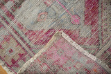 Distressed Oushak rug corner revealing worn pink pile, secured selvage, and hand knotted foundation.