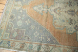 Distressed Oushak rug corner, showing worn pile, fringed edge, and pale sandalwood with mint green.