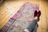 Distressed vintage Oushak runner showcasing a diamond medallion and playful pink and blue shades.