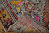 Distressed Oushak rug runner pile with pink, yellow, blue, and aubergine colors, revealing foundation and original selvage.
