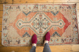 Distressed vintage Oushak rug's central medallion with stepped contour, brick red field, and lattice spandrels.