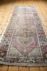 Distressed Oushak runner's fringed end, with faded mauve, green, and ivory tones.