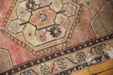 Distressed Oushak rug detail: hexagonal medallion, vinery, seed motifs in faded apricot mauve, ivory.