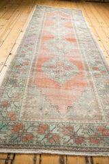 Patinaed Oushak runner end, floral pinwheel border in apricot, mint, charcoal, and fringe.