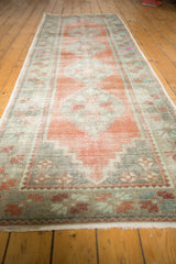 Distressed vintage Oushak runner end, terracotta and mint floral pinwheel motifs, showing wear.
