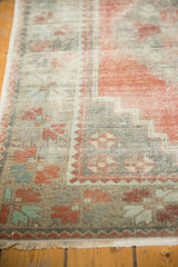 Distressed Oushak rug corner with textured pile, fringe, apricot, charcoal, and mint green colors.