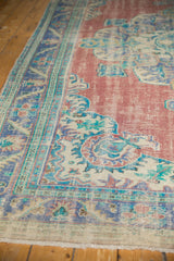 Distressed Oushak carpet: worn brick red field, blue border, ivory medallion, and fringed edge.