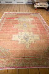 Abrashed blush field and primitive rams horn design motif on a distressed vintage Oushak rug.