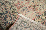 Distressed vintage Oushak rug corner showing blush, charcoal motifs, fringe, and visible foundation.