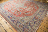 Distressed Oushak rug corner showing faded red vinery, royal blue floral border, and worn pile.