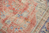 Vintage distressed Oushak carpet detail, showing worn pile, visible foundation, faded red and blue patterns.