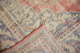 Distressed vintage Oushak carpet corner, showing faded cherry red, ivory, royal blue, and visible foundation.