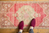 Distressed Oushak runner, faded bubble gum pink field, antique ivory floral medallion, visible wear.