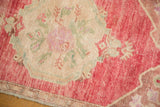Distressed Oushak rug corner: bubble gum pink field, ivory floral, and intact selvage.