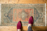 Distressed vintage Oushak rug corner, revealing dusty terra cotta, teal geometric vinery, and soft fringe.