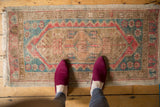 Distressed Oushak rug corner showing geometric lozenge and floral motifs in cherry red and teal.
