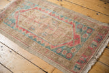 Distressed Oushak rug corner showing dusty teal floral cross sections and blush cherry red vine border.